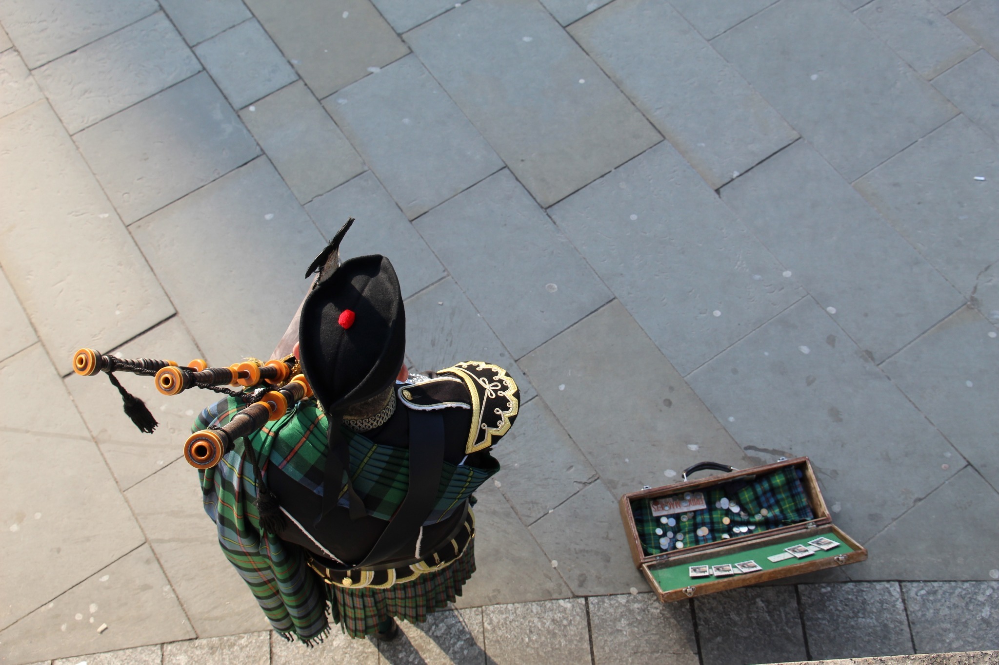 An aerial view of a bagpipe player busking and wearing a Glengarry hat An aerial view of a bagpipe player busking and wearing a Glengarry hat
