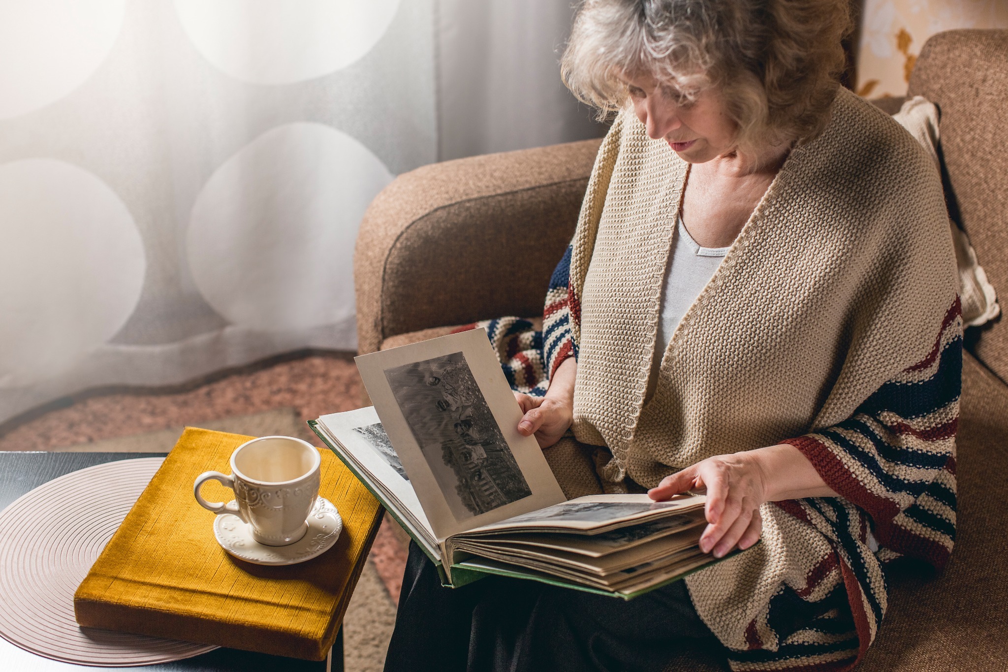 A elderly woman experiencing Hiraeth (the Welsh word for nostalgia) while looking at a photo album and having tea. A elderly woman experiencing Hiraeth (the Welsh word for nostalgia) while looking at a photo album and having tea.