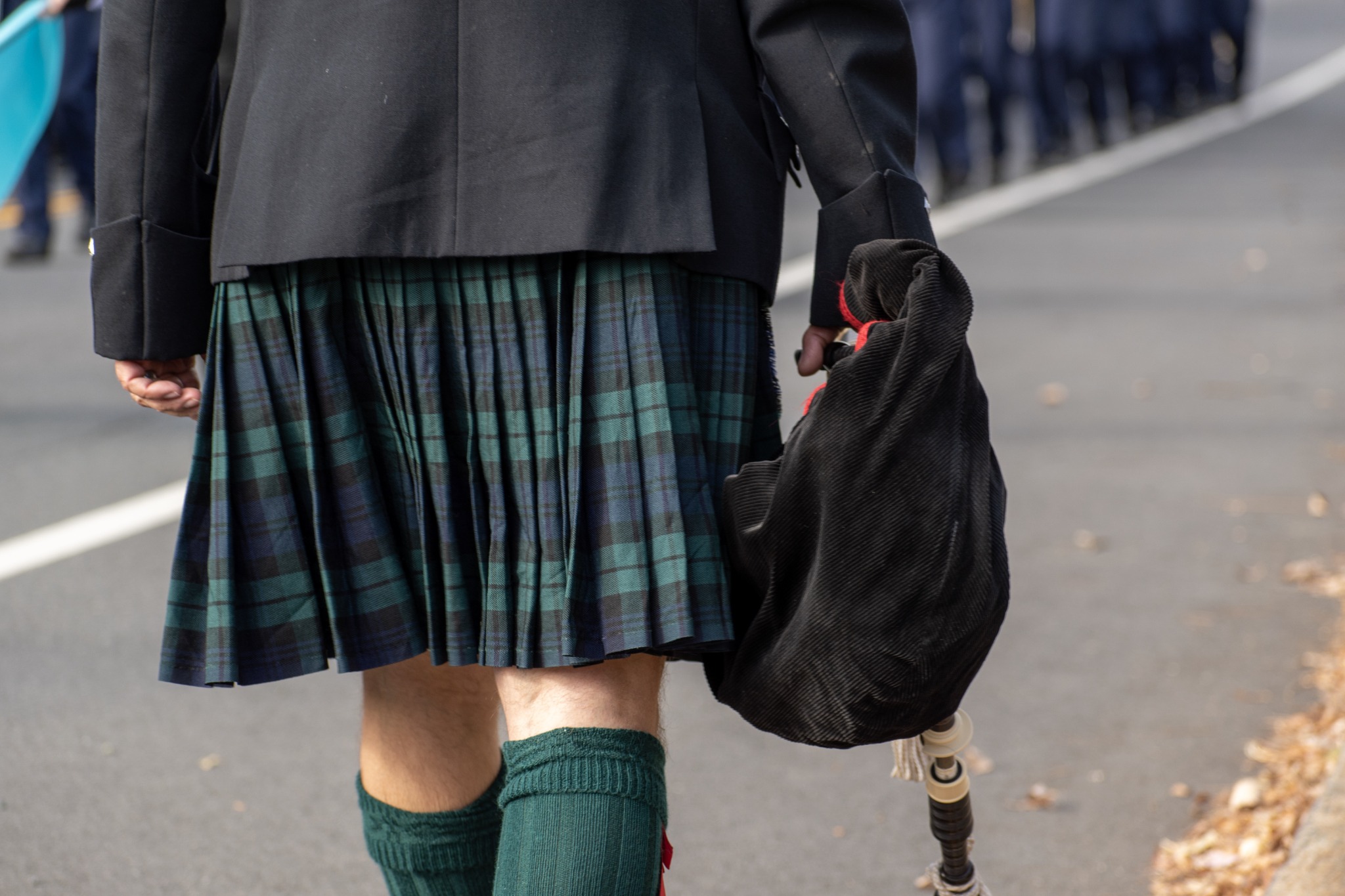 A shot of a man walking away wearing a green and blue tartan kilt and holding a bagpipe.