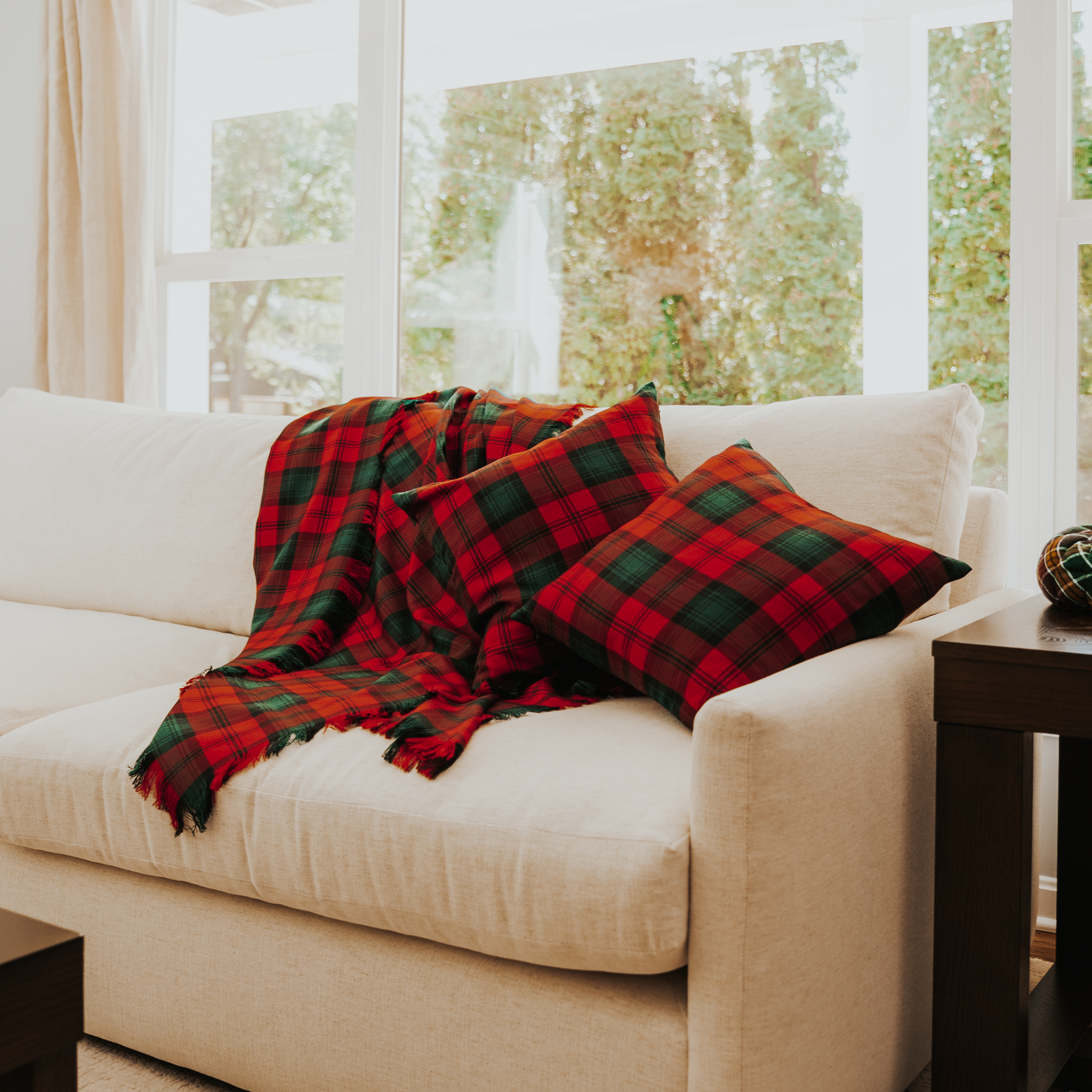 A green and red tartan pillow and blanket set resting on a cream coloredcouch.