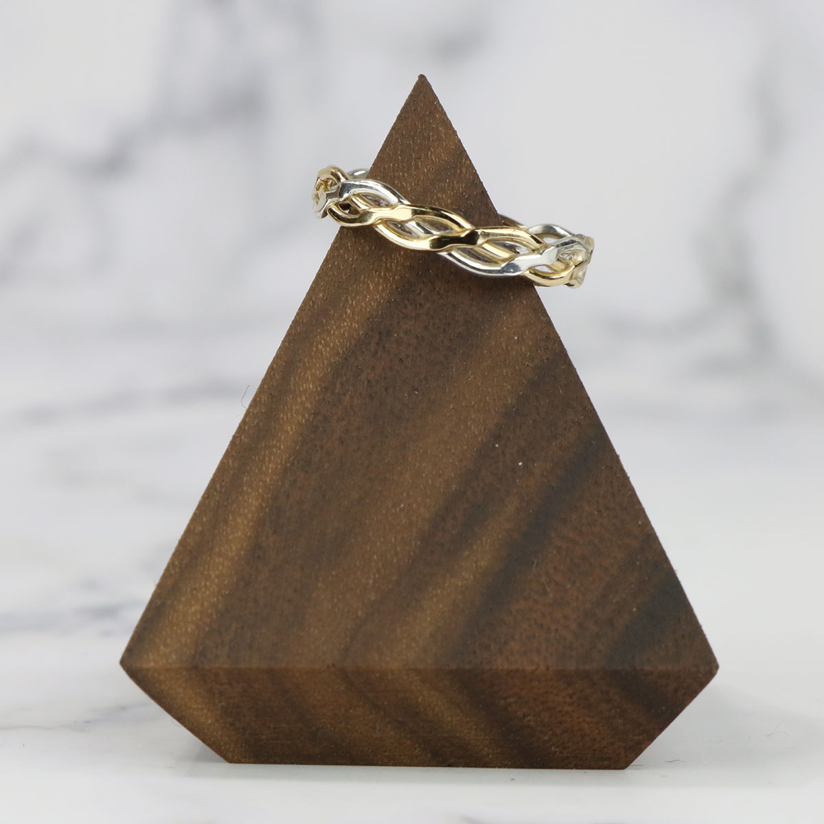 A Celtic Wedding Band on a wooden triangle for display. It is a two-metal Celtic knot design.