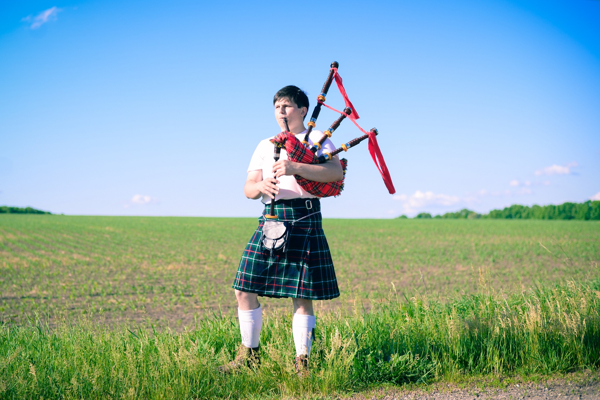 A young man playing a bagpipe in a field in Scotland.