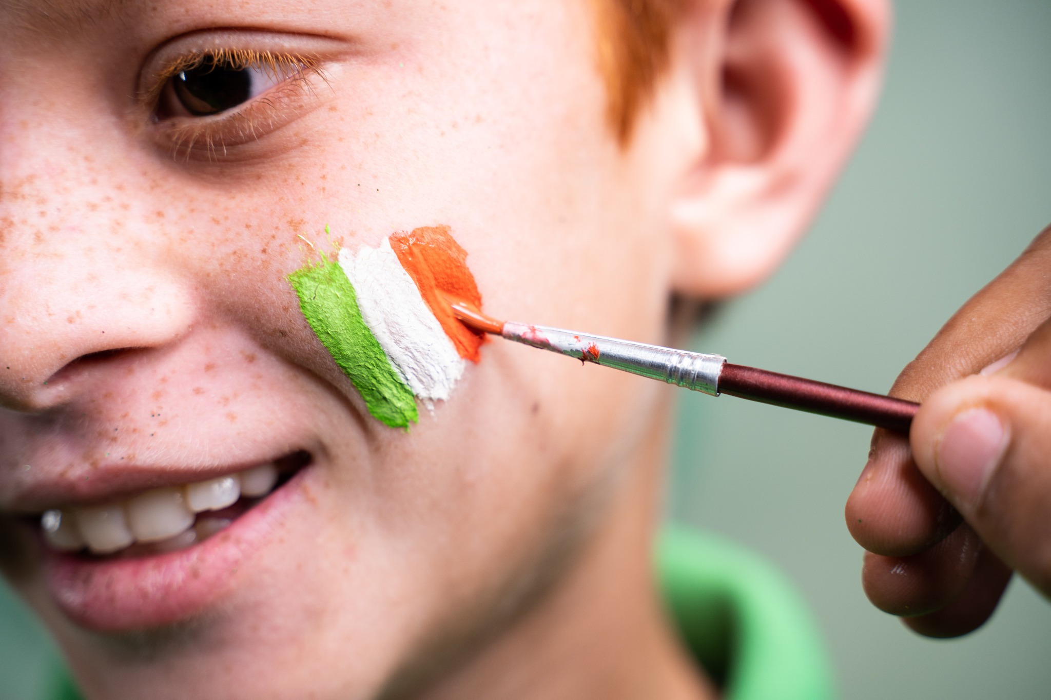 A red-headed child having the Irish flag painted on his cheek.