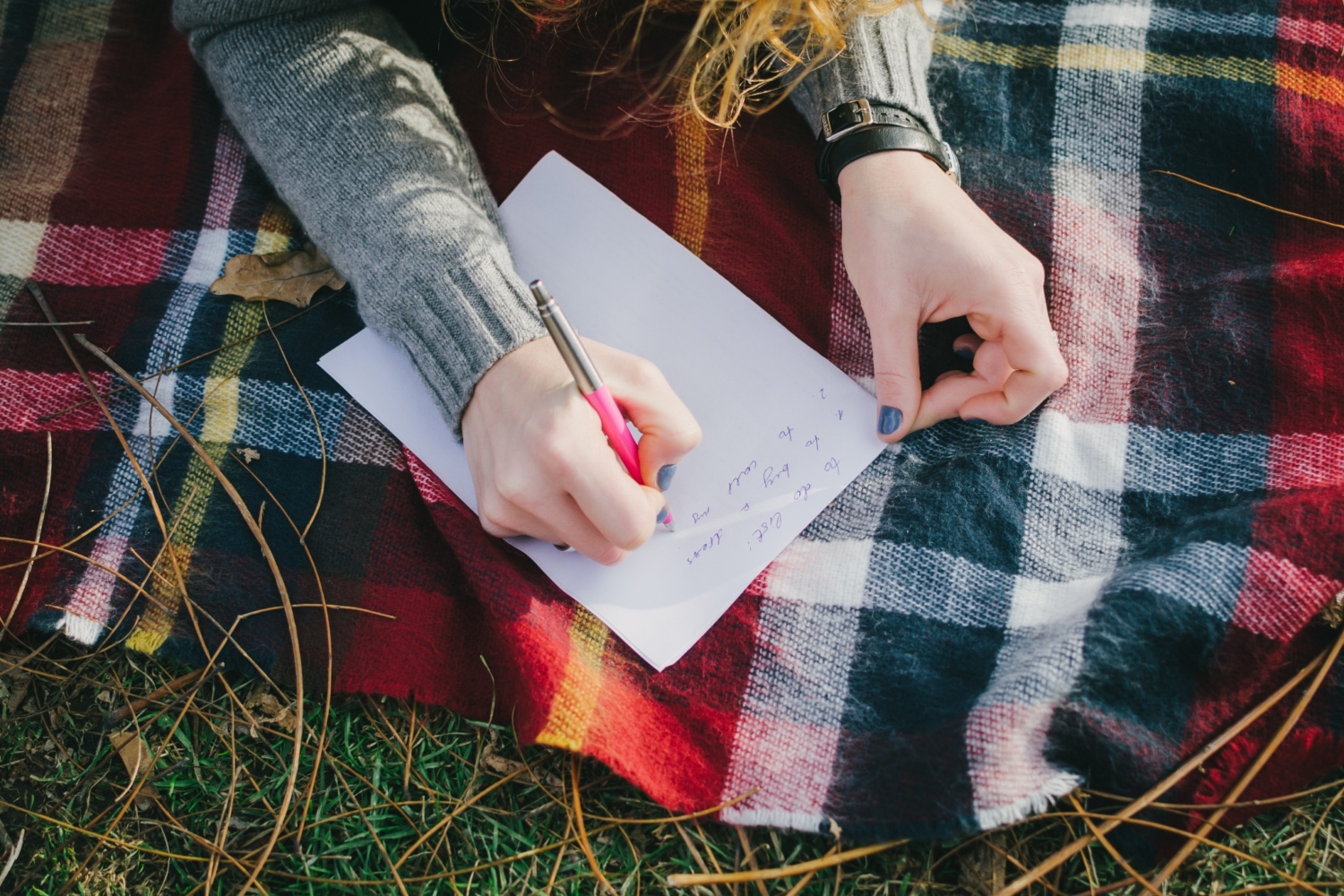 A person journaling outdoors while laying on a tartan blanket to reflect during Beltane.