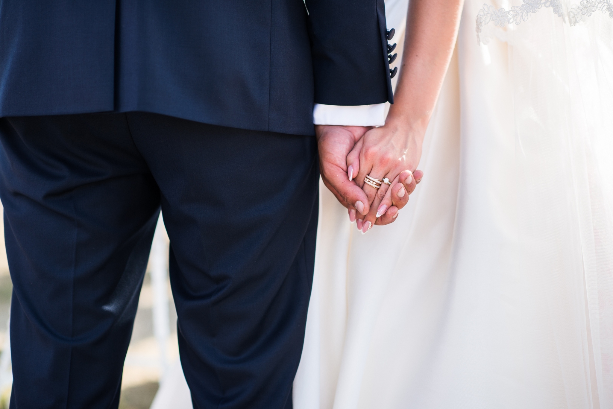 A couple holding hands on their wedding day and wearing wedding rings.